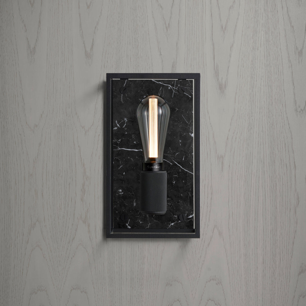 Buster and Punch caged wall lamp medium i sort metal med bagpanel i sort marmor.