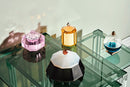 Fire forskellige duftlys i farvet krystal, stående på indskudsborde i glas.