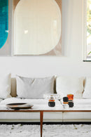 Opstilling af lysestager og skål i farvet krystal, på sofabord i marmor med sofa og kunst i baggrunden.