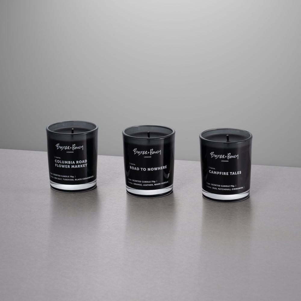 3 duftlys af sort voks i røgfarvede glas, på grå baggrund.