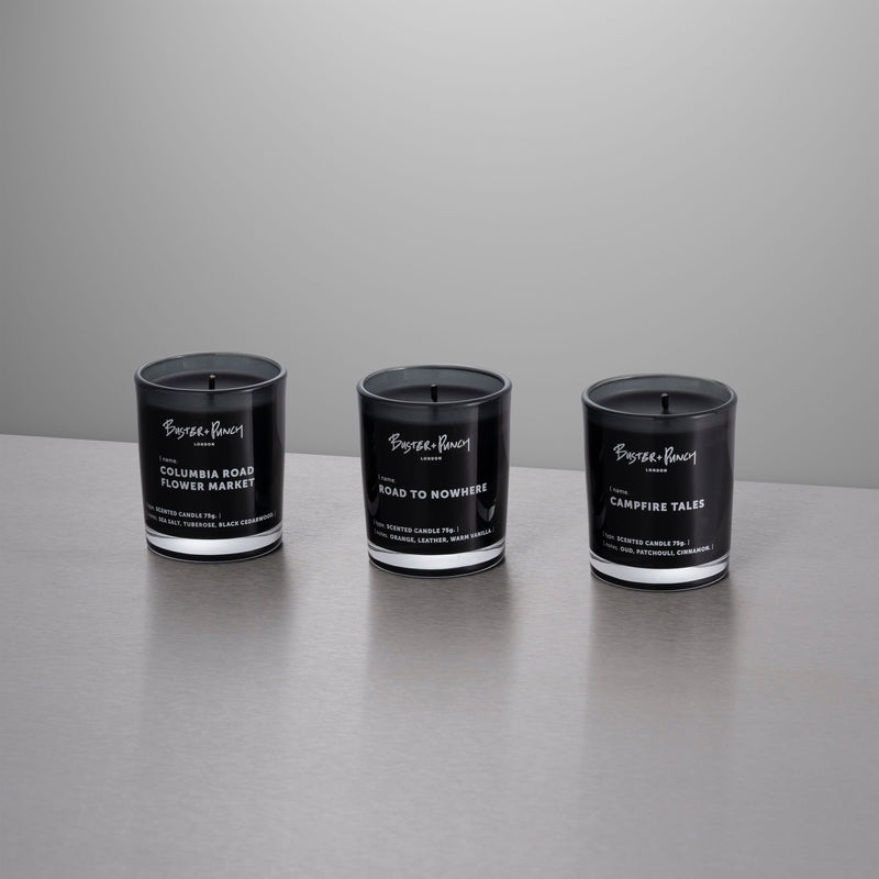 3 duftlys af sort voks i røgfarvede glas, på grå baggrund.