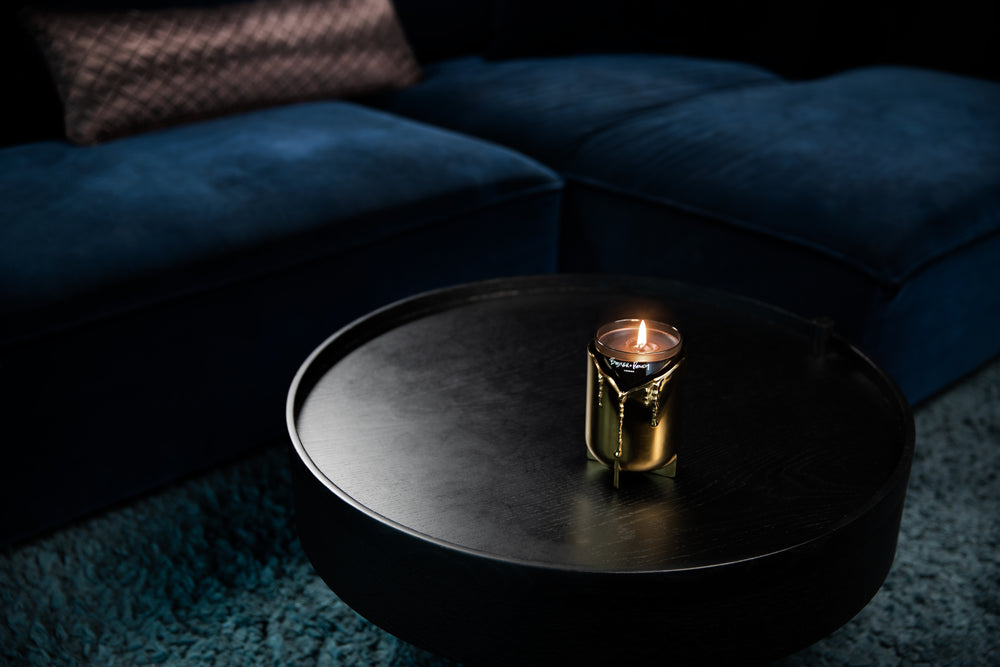 Lystage i messing med duftlys i glas, stående på sort sofabord.