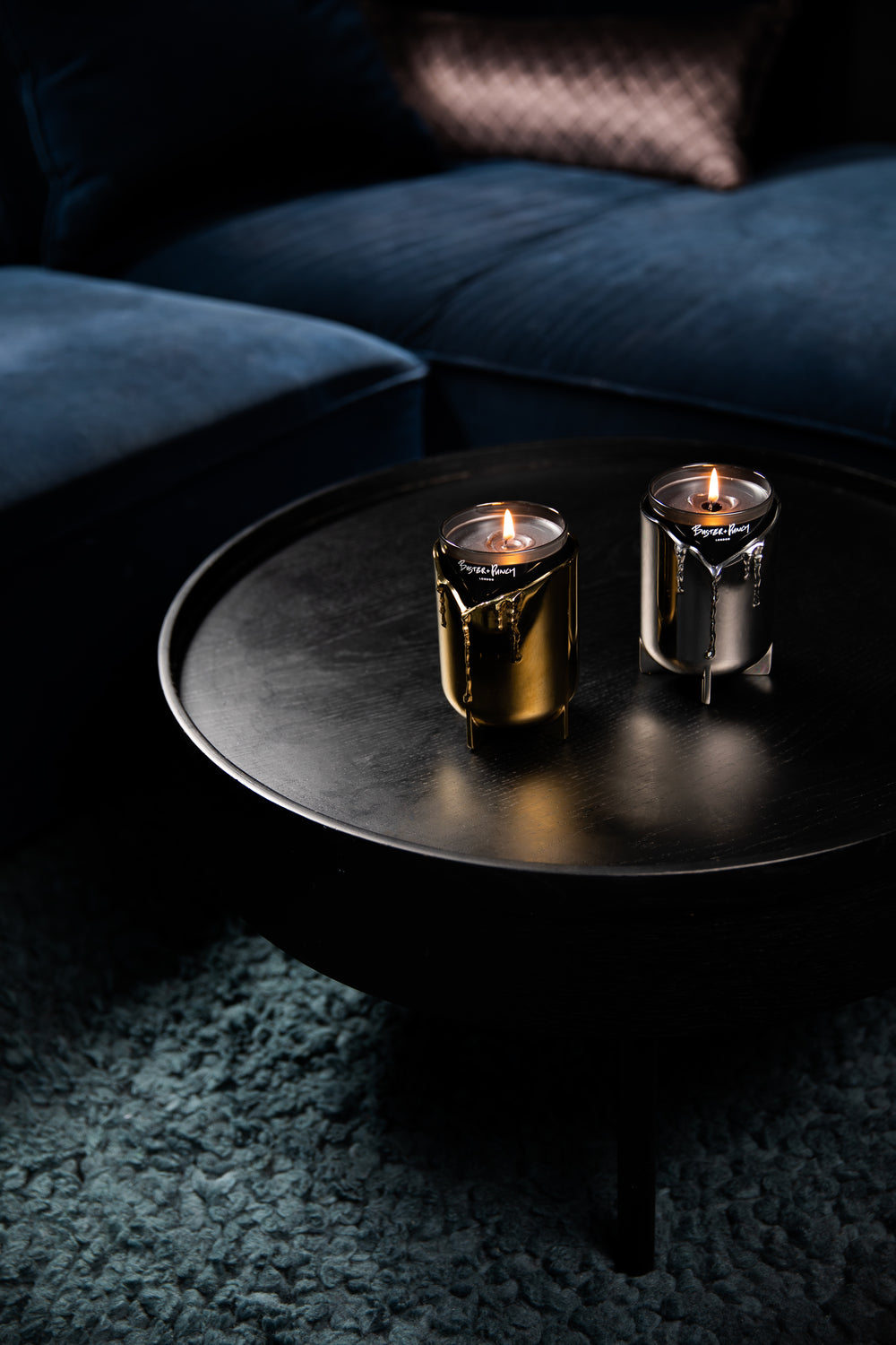 2 lystager i messing og stål med duftlys i glas, stående på sort sofabord.