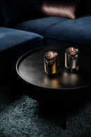 2 lystager i messing og stål med duftlys i glas, stående på sort sofabord.