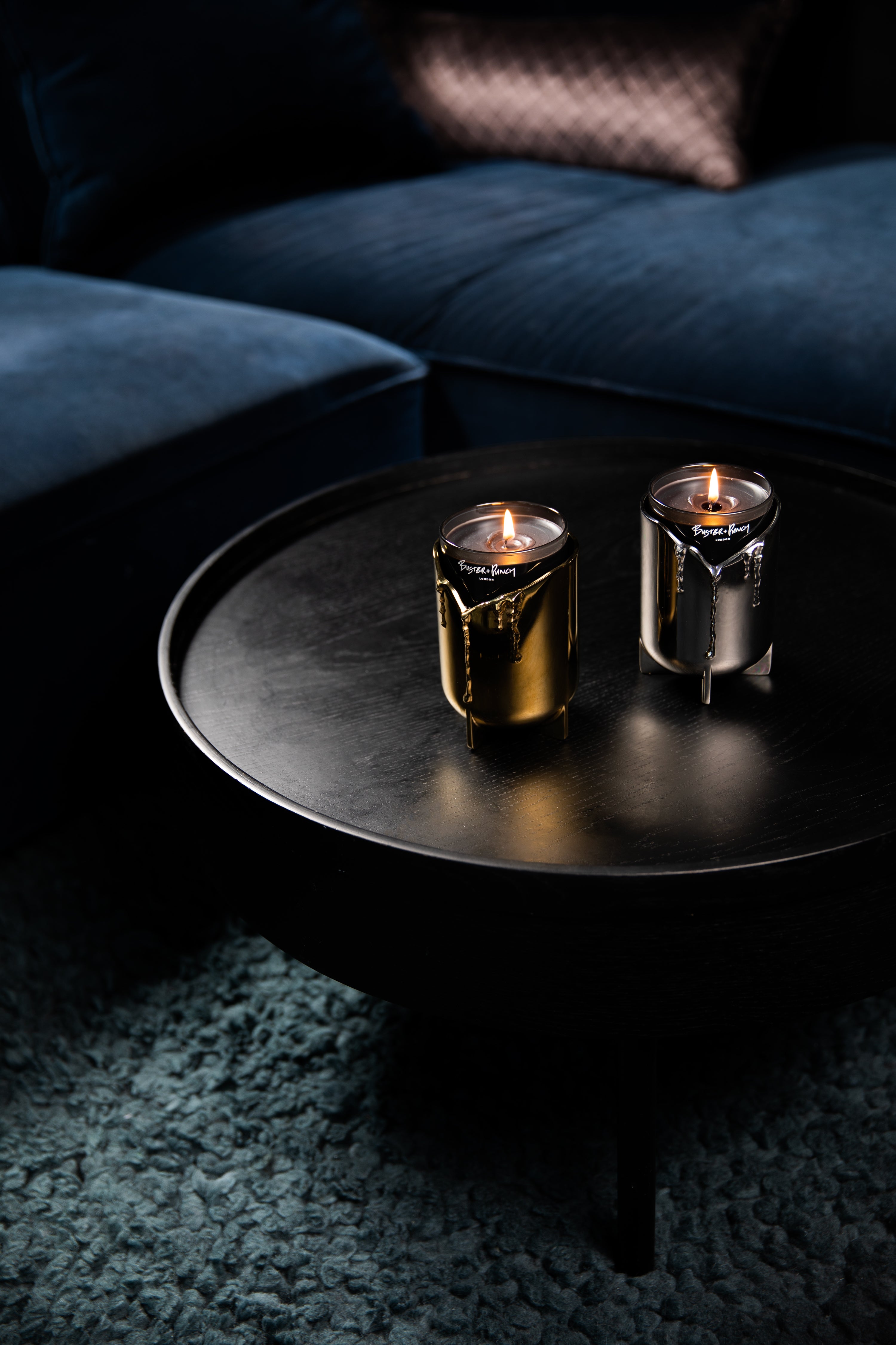 2 lysestager i stål og messing med duftlys i glas, på sort sofabord