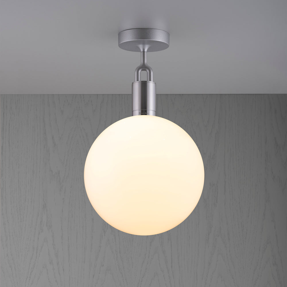 Loftlampe med rund skærm af opalglas og stålfatning, på baggrund af grå trævæg.
