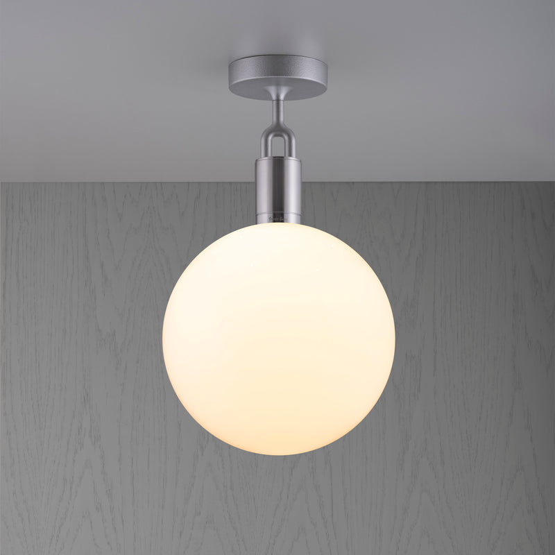 Loftlampe med rund skærm af opalglas og stålfatning, på baggrund af grå trævæg.