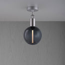 Loftlampe med rund skærm af røgfarvet glas og fatning i stål, på baggrund af gråt træ