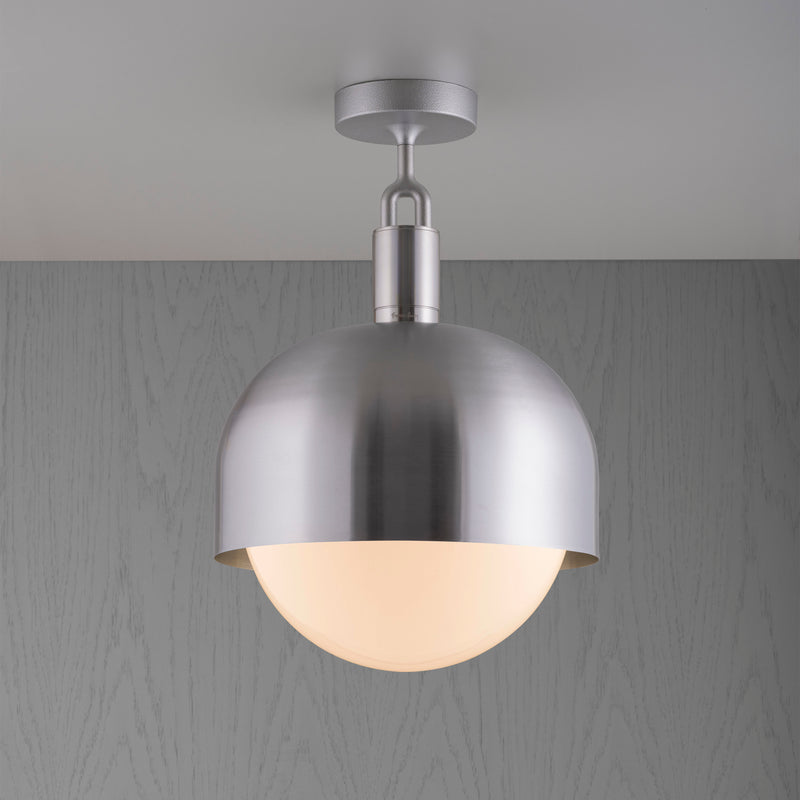 Loftlampe med fatning og skærm i stål samt pære i opalglas, på grå baggrund.
