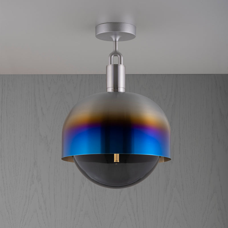 Loftlampe med fatning af stål samt skærm af brændt stål og pære af røgfarvet glas, på grå baggrund.