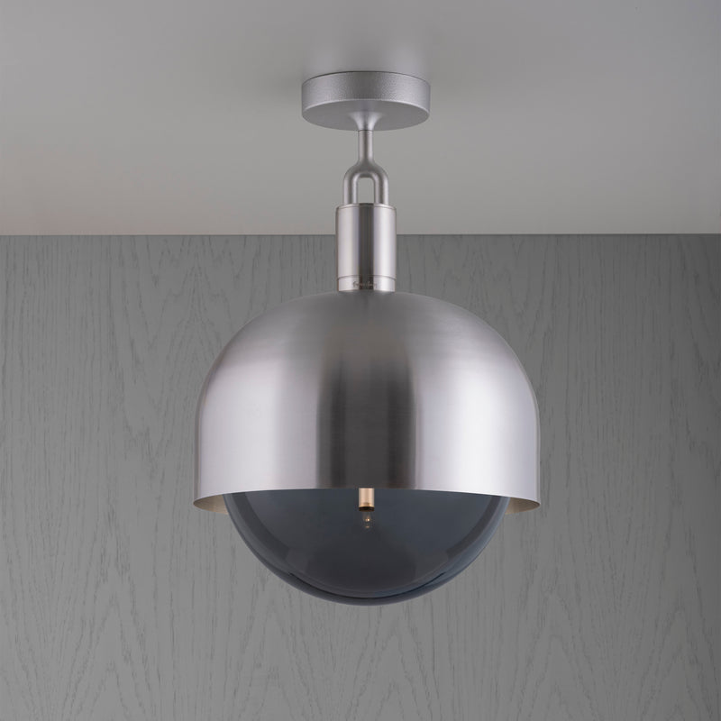 Loftlampe med fatning og skærm af stål samt pære i røgfarvet glas, på grå baggrund.