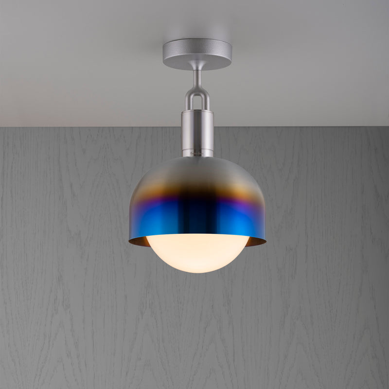Loftlampe med fatning i stål samt skærm i brændt stål og pære i opalglas, på grå baggrund.
