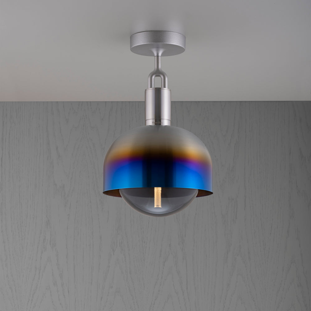 Loftlampe af stål og skærm af brændt stål samt røgfarvet pære, på grå baggrund.
