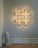 Væglampe med lampeskærme af klart optikglas og gylden fatning og stel, på hvid væg