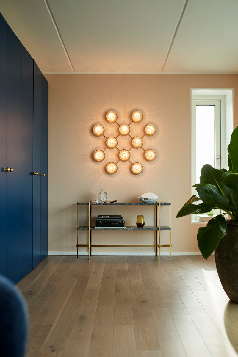 Væglampe med lampeskærme af klart optikglas og gylden fatning og stel, på beige væg i soveværelse