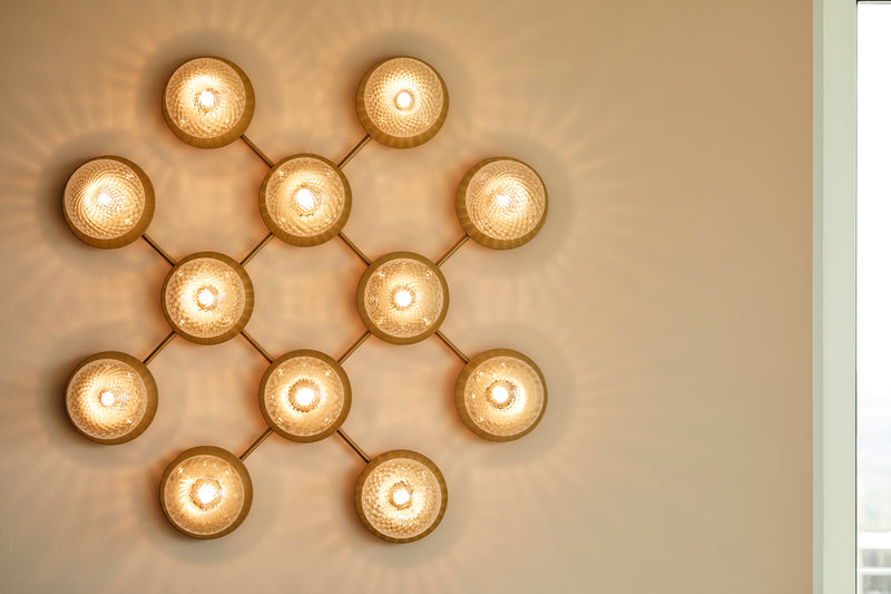Væglampe med lampeskærme af klart optikglas og gylden fatning og stel, på beige væg