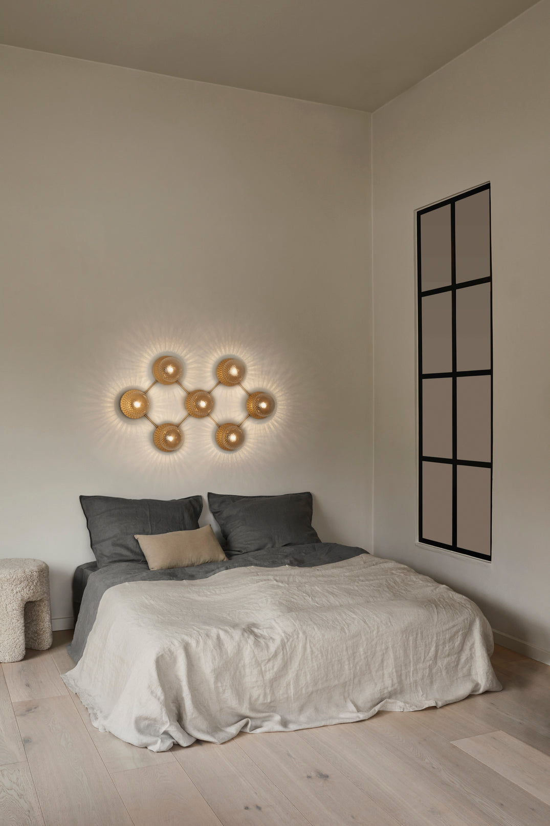 Væglampe med lampeskærme af klart optikglas og gylden fatning og stel, hængende over seng i soveværelse