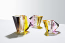 Opsætning af vaser i klar, brun, gul og lyserød krystal. samt bonbonniere og to lysestage, på hvidt bord og hvid baggrund.