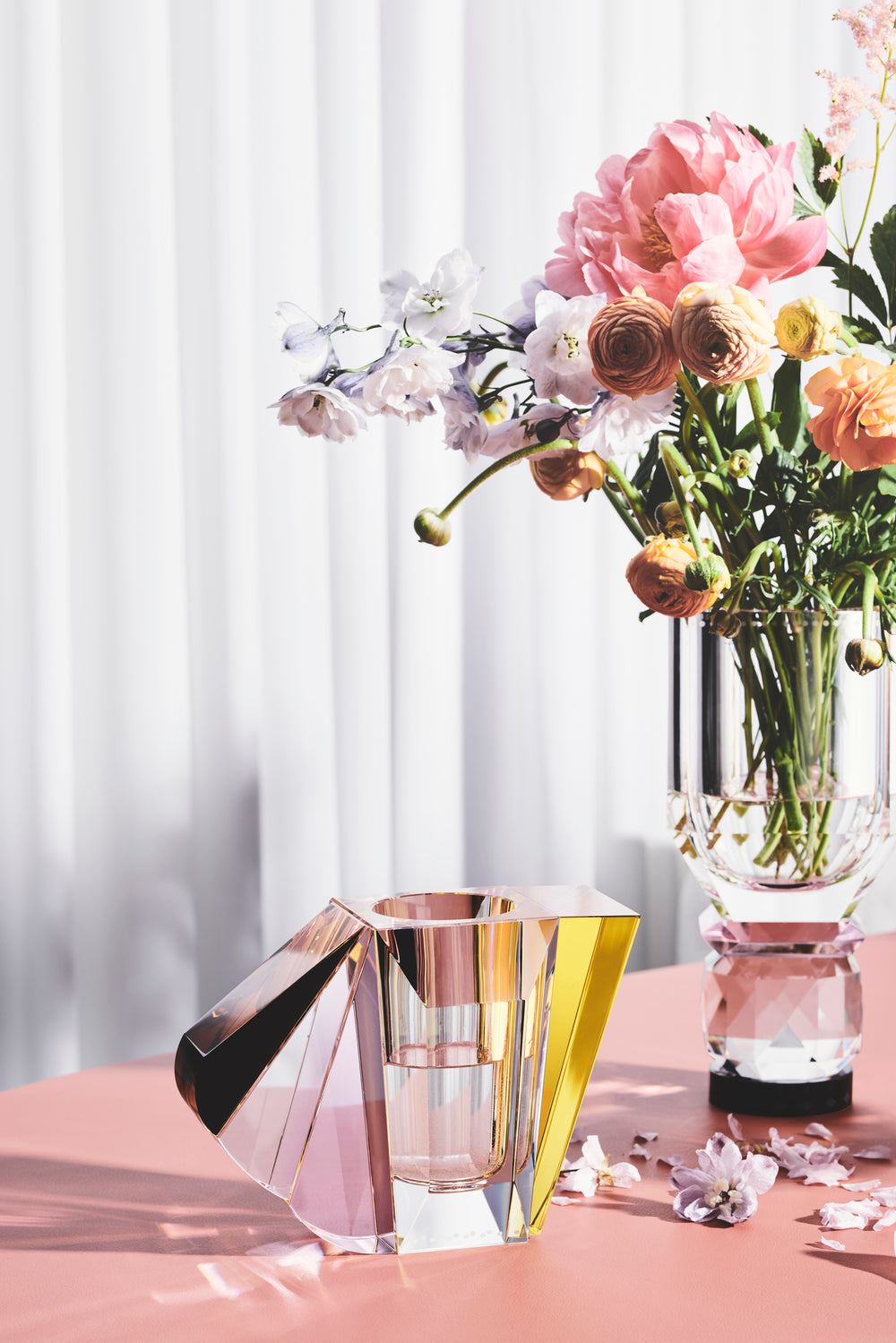 Opsætning af vaser i klar, brun, gul og lyserød krystal med blomster i, på bord med koralfarvet dug.