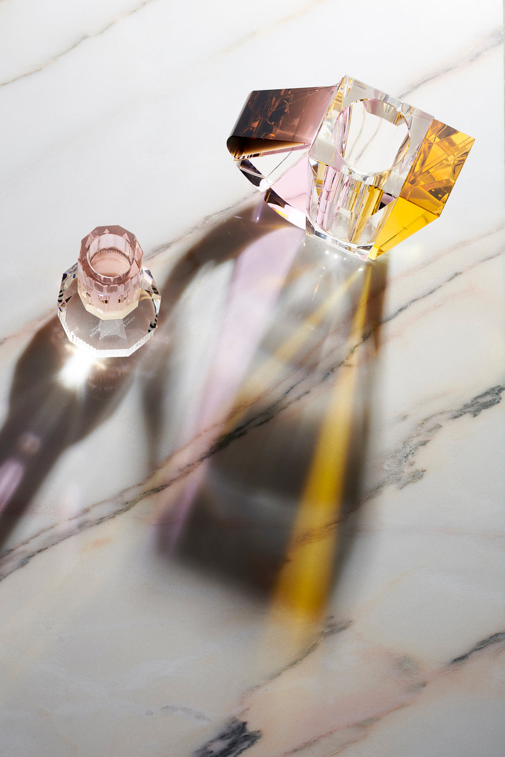 Opsætning af en vase i klar, brun, gul og lyserød krystal. samt en lysestage set oppefra, på marmor bordplade.