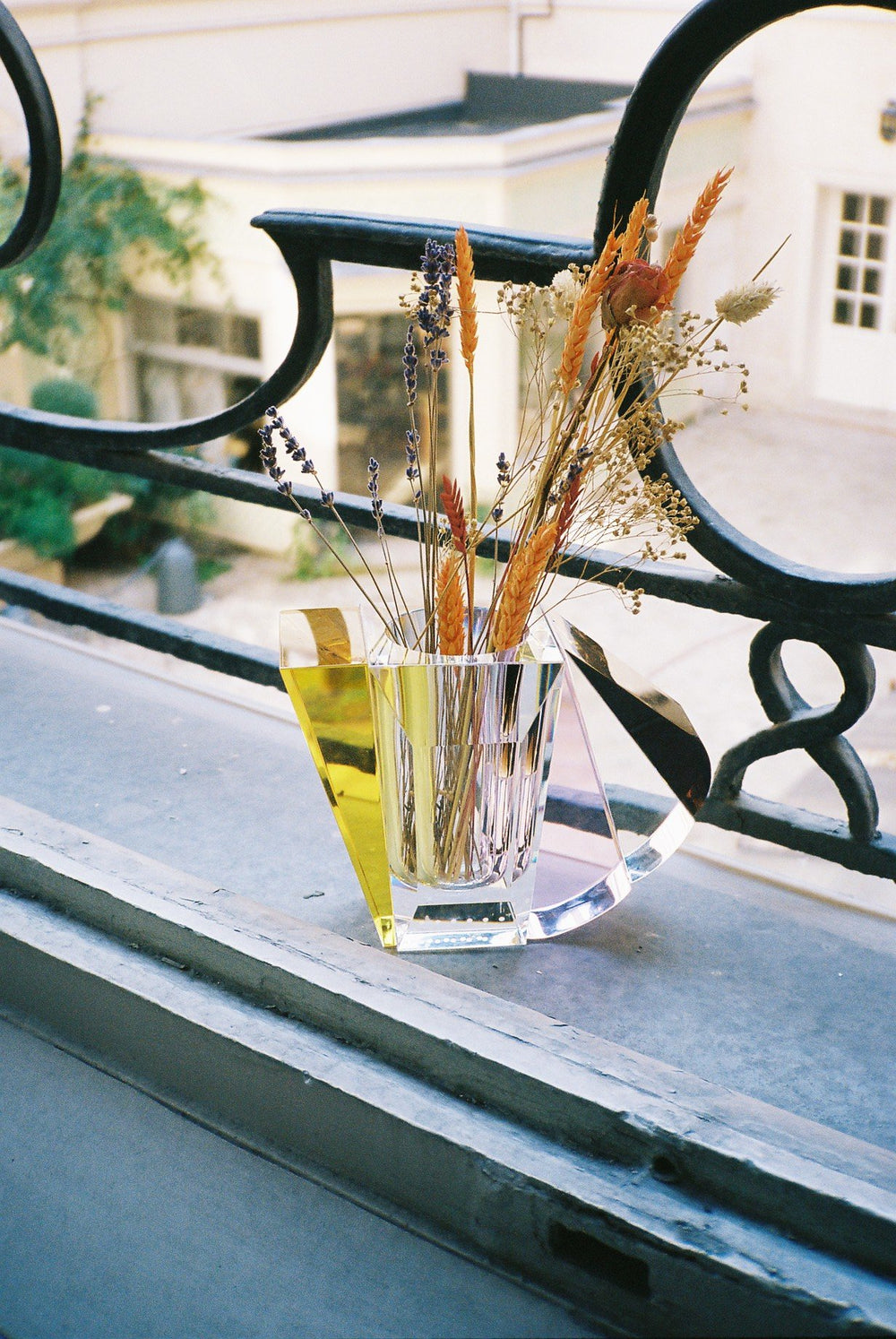 Vase i klar, brun, gul og lyserød krystal med blomster i stående på altan.