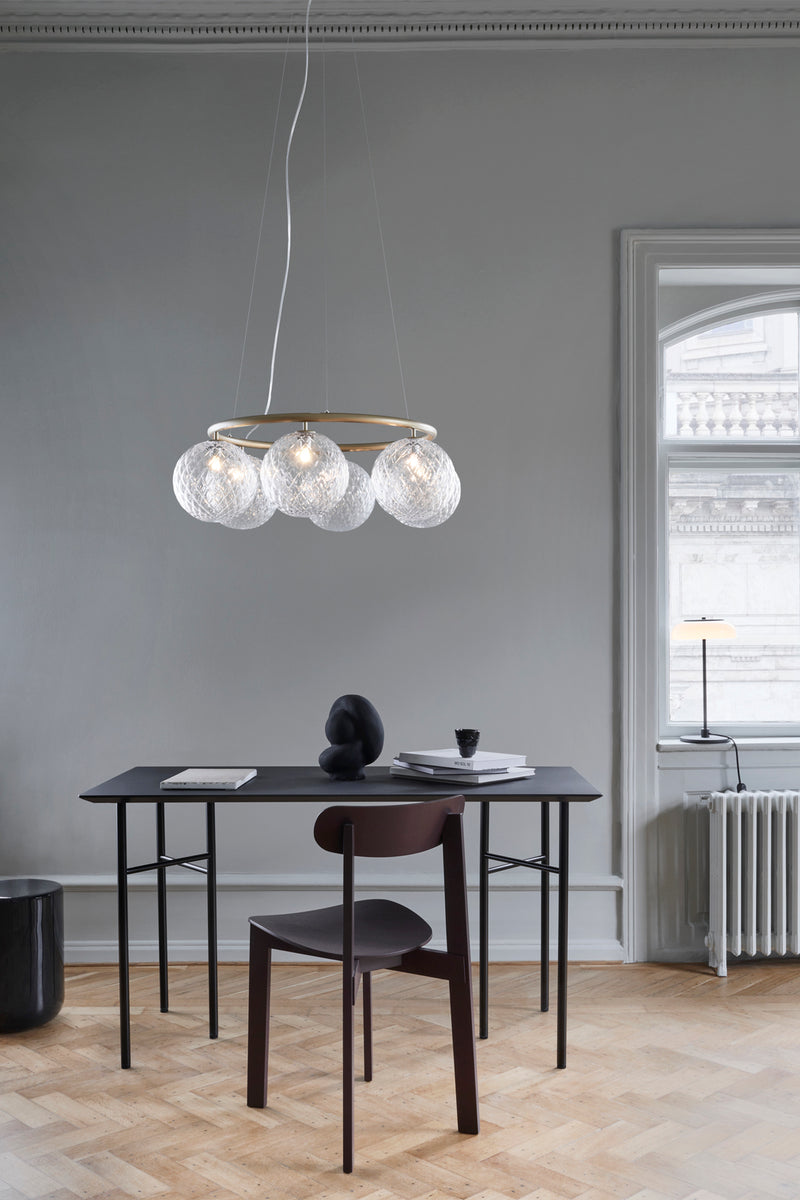 Lysekrone bestående af seks runde skærme i klart optikglas samt messingfarvet krone, over skrivebord