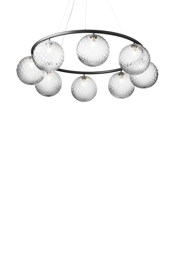Lysekrone bestående af otte runde skærme i klart optikglas samt krone i mørkegrå, på hvid baggrund