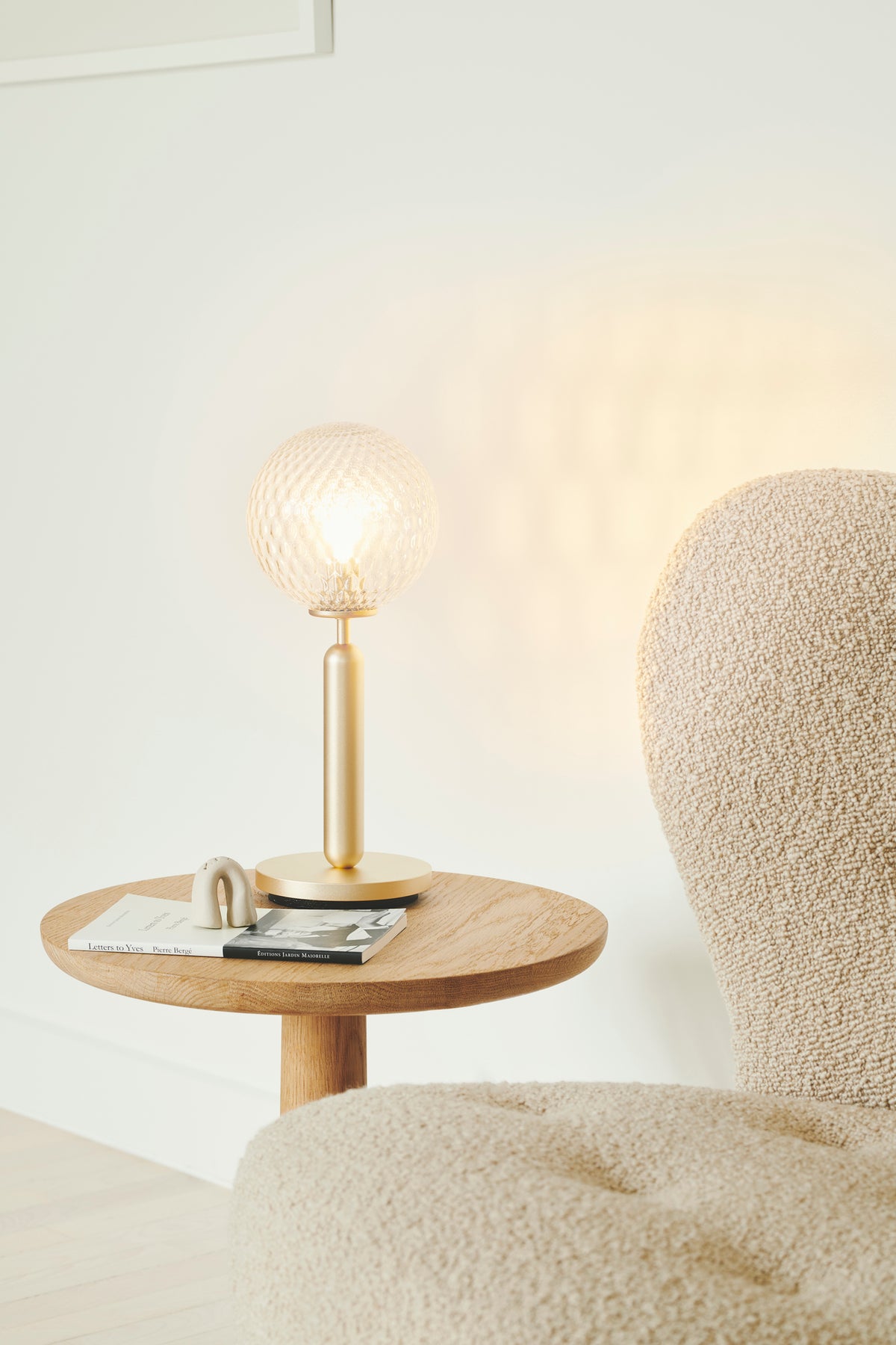 Bordlampe med rund skærm af klart optikglas og mørkegråt stel, på sidebord i dagligstuemiljø