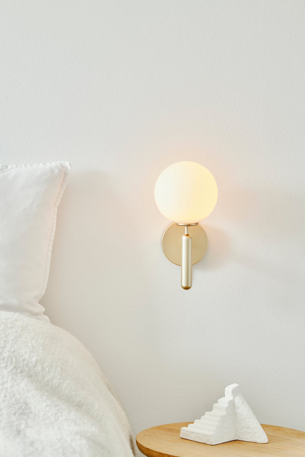 Væglampe med rund skærm af opalglas og messingfarvet stel, placeret i soveværelse
