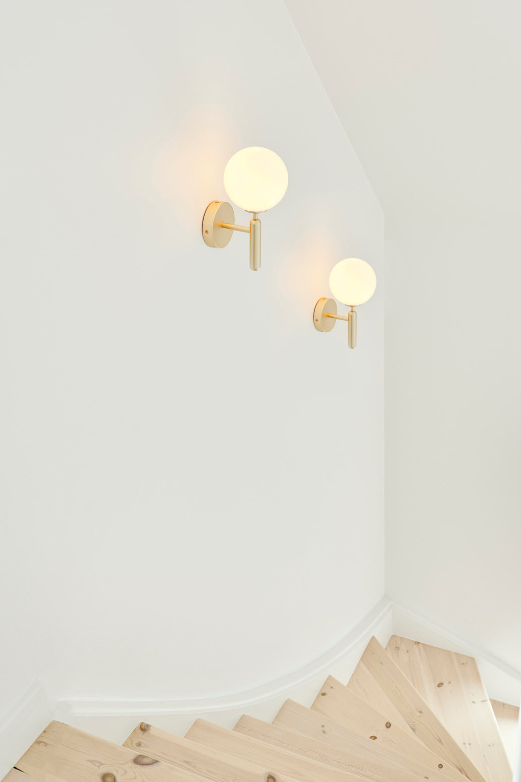 Væglampe med rund skærm af opalglas og messingfarvet stel, placeret langs trappe