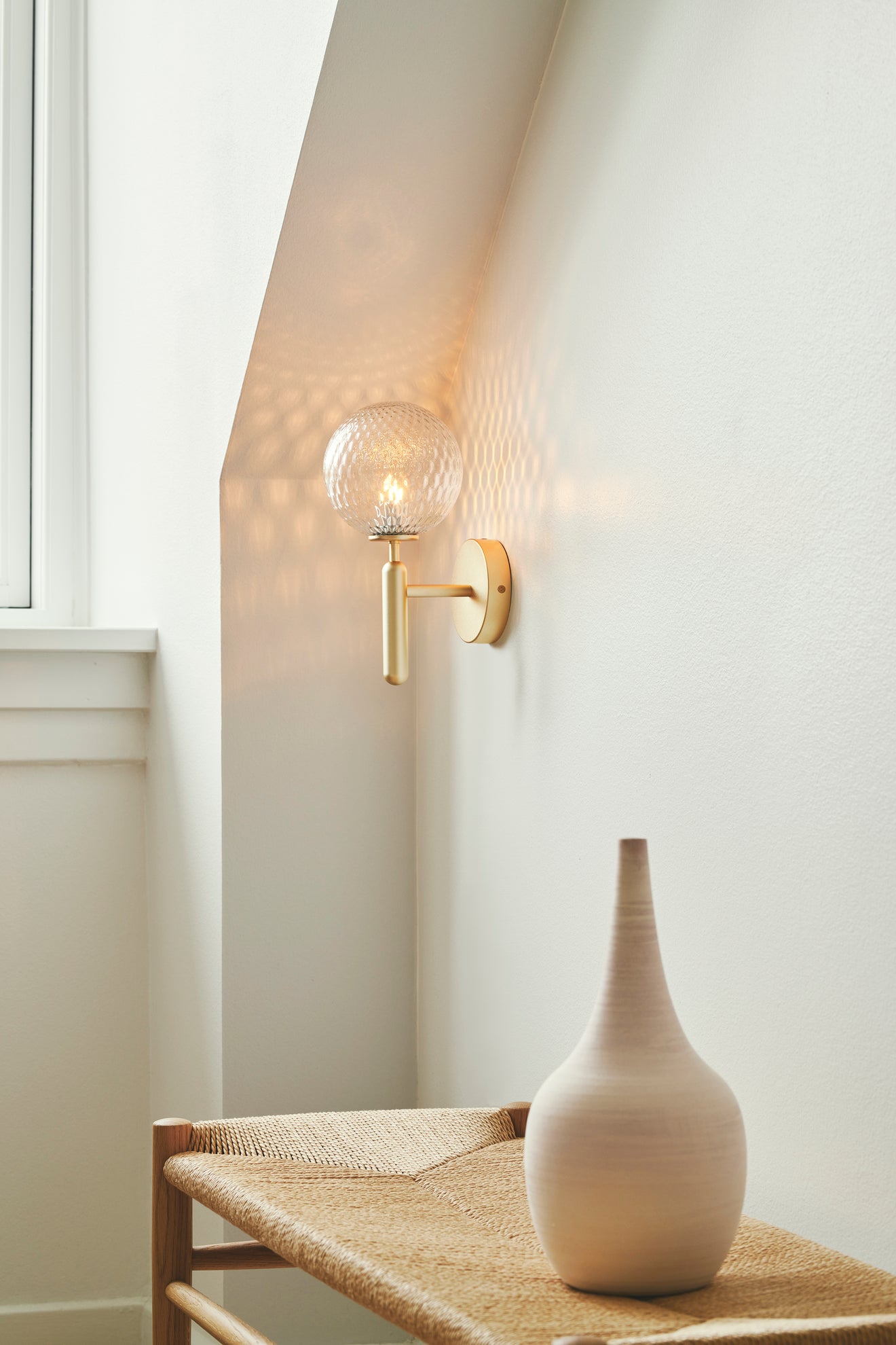 Væglampe med rund skærm af klart optikglas og messingfarvet stel, i dagligstuemiljø