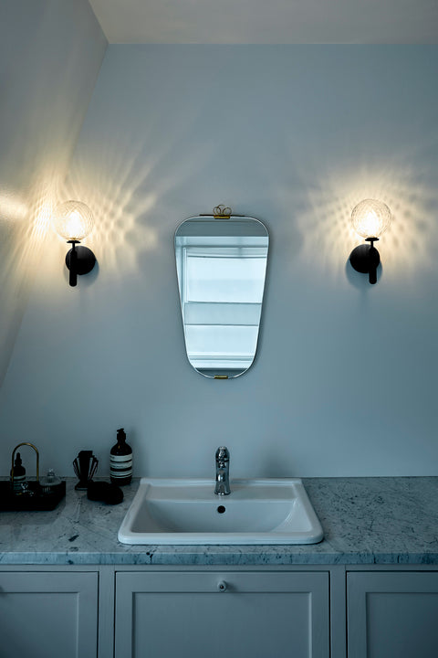 Væglampe med rund skærm af klart optikglas og mørkegråt stel, på badeværelse