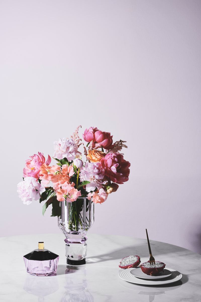 Opstilling af vase med blomster og bonbonniere på hvidt marmorbord med lyserød baggrund.