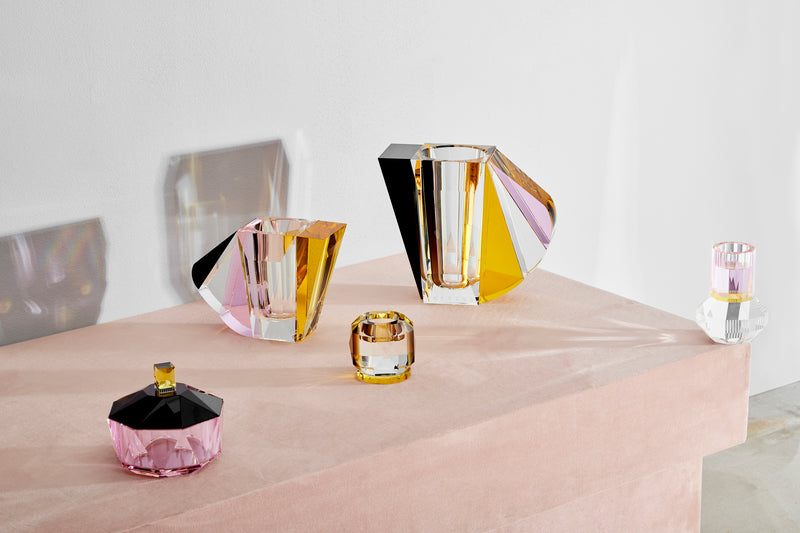 Opstilling af vaser, lysestager samt bonbonniere i farvet krystal, på lyserødt bord med hvid baggrund