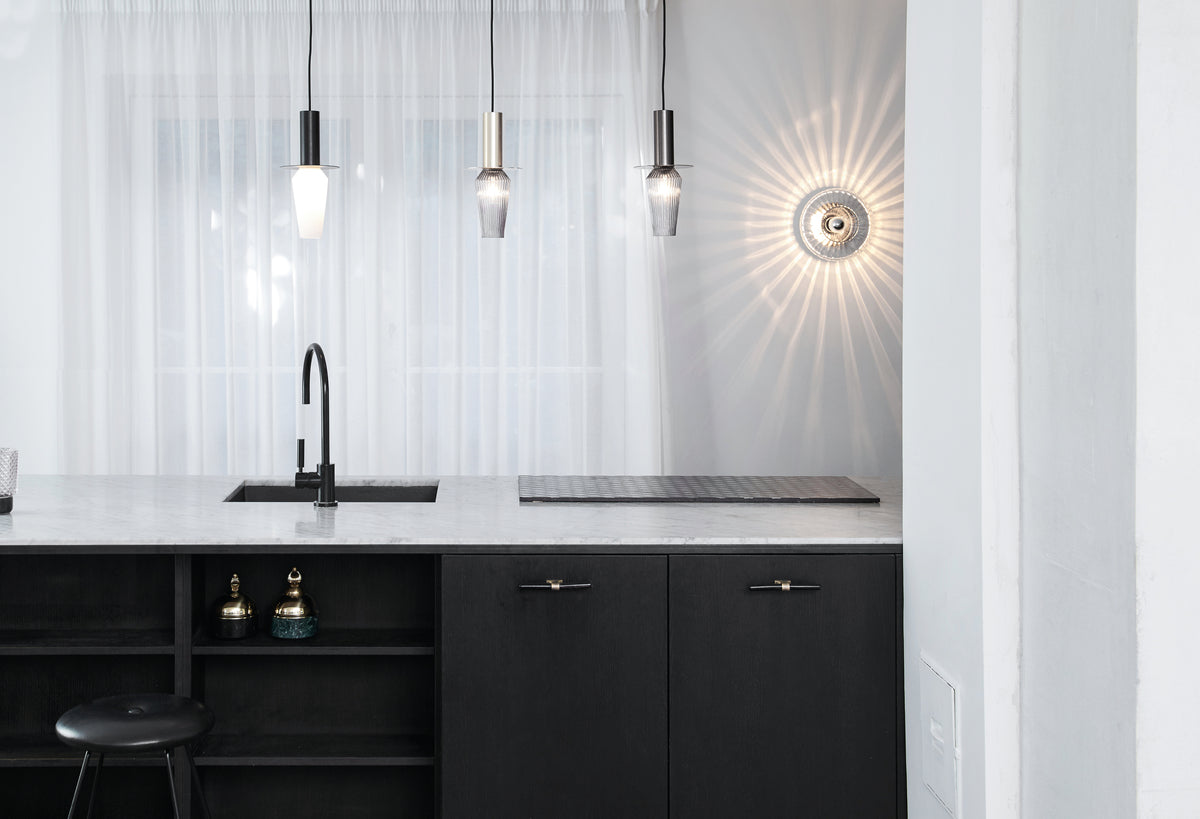 Rund væglampe i klart plisseret glas, som skaber et lysspil på væggen