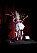 Opstilling af fyrfadsstager og vase med blomster, i farvet krystal på sort bord og rød baggrund.