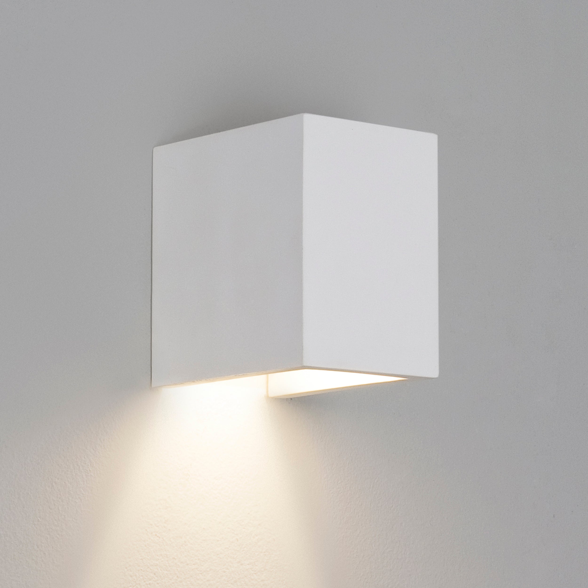 En lille hvid og enkel væglampe i firkantet form fremstillet i gips med nedadgående lys.