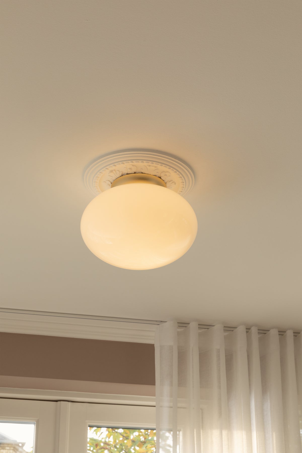 Loftlampe med messingfarvet fatning og skærm i opalglas, i dagligstuemiljø