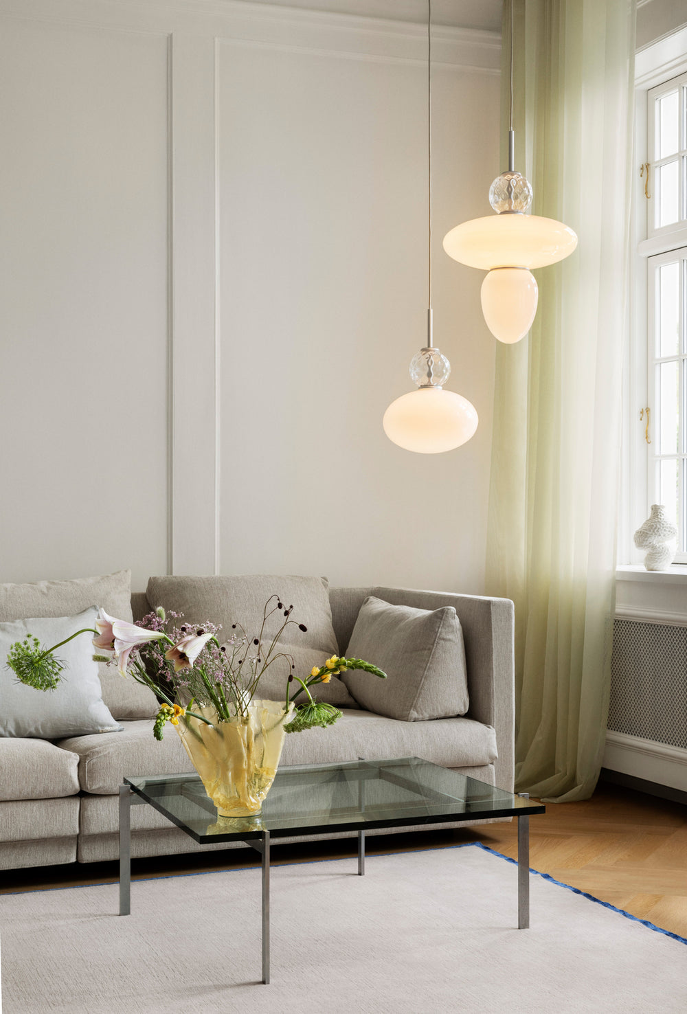 Pendler bestående af to glasskærme, én i klart optikglas og én i opalglas samt sølvfarvet ophæng, i dagligstuemiljø