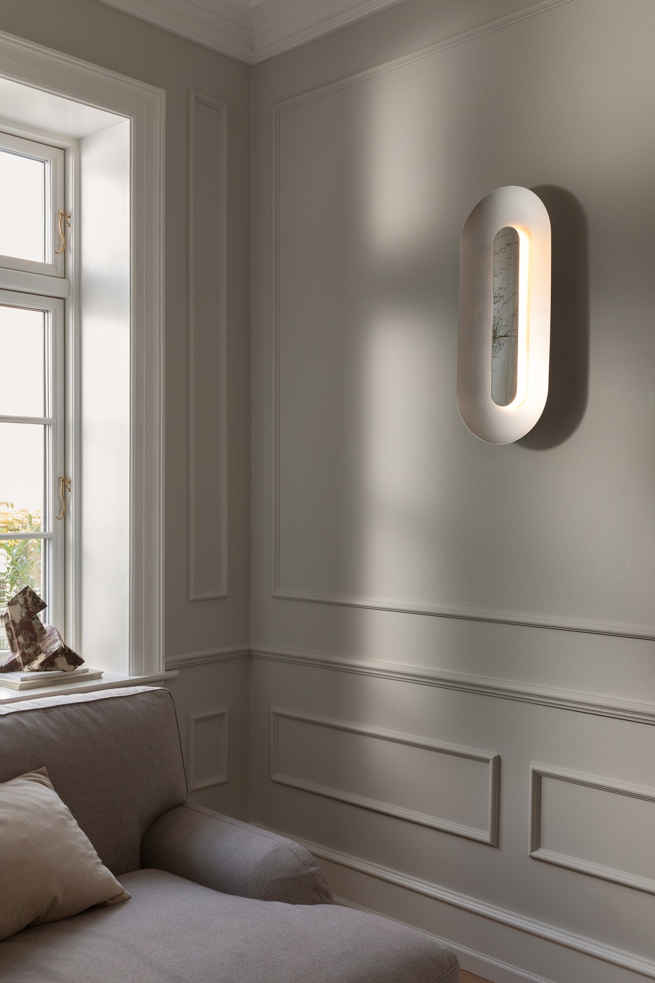 Oval sølvfarvet væglampe med indirekte lys, i dagligstuemiljø