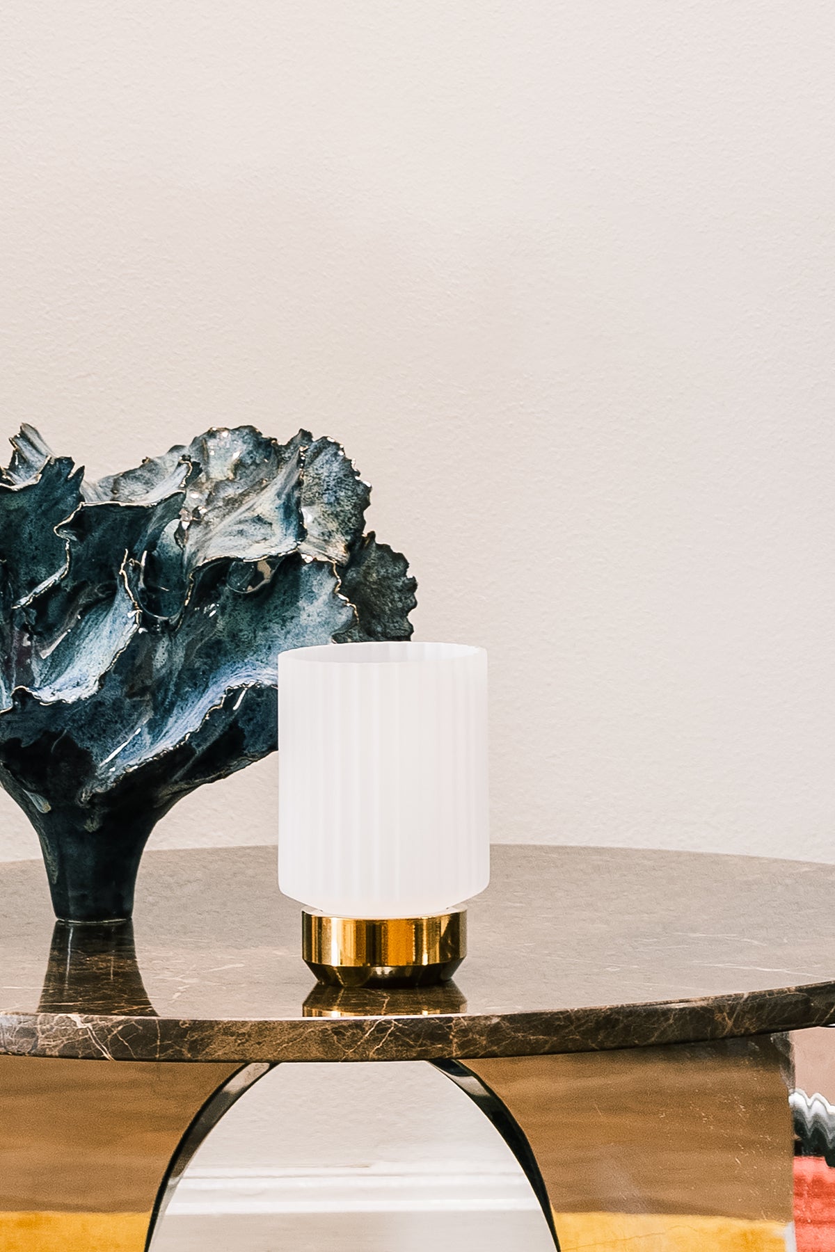 Fyrfadsstage af messingfod og hvidt linjeret opalglas, på bord af brun marmor og med skultur i baggrunden