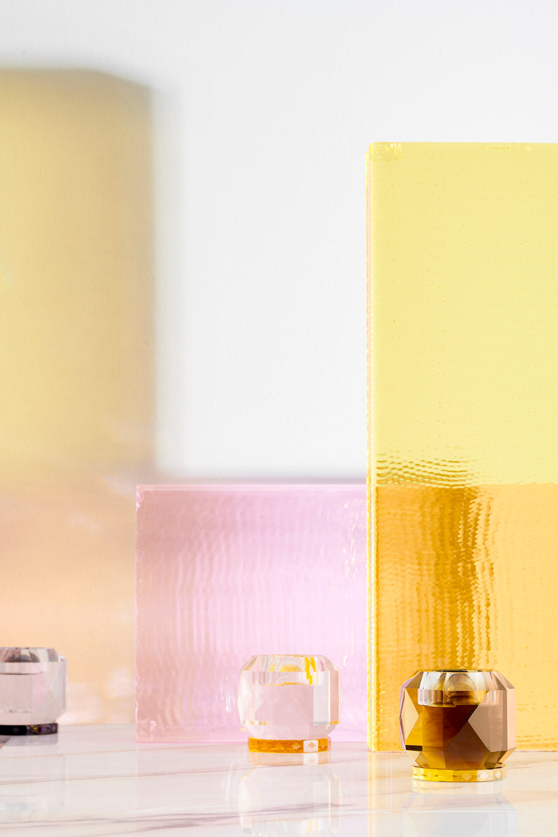 Opstilling af tre fyrfadsstager i farvet krystal, med farvede glasplader i baggrunden.