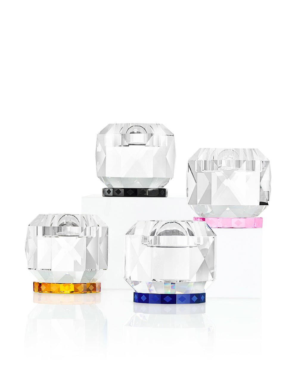 Fire fyrfadslysestager i klart og farvet krystal, på hvid baggrund.