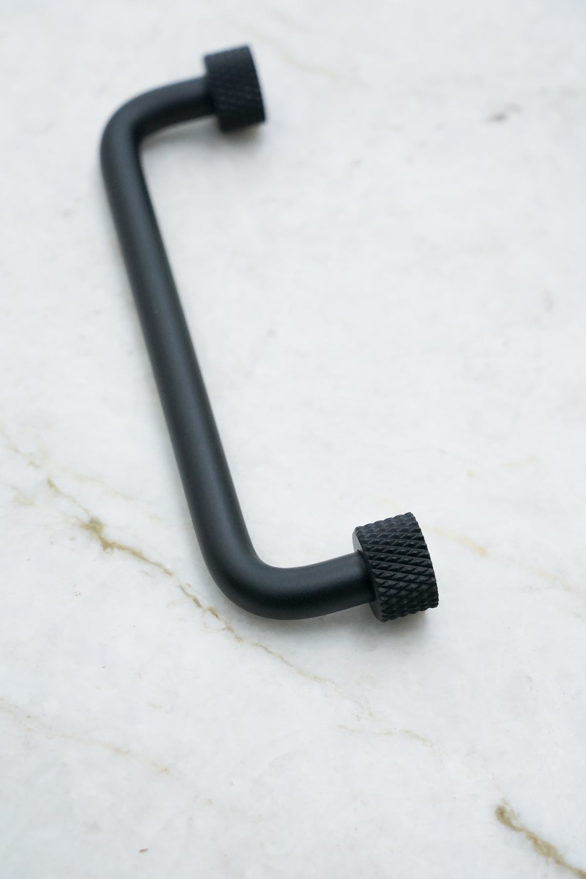 Køkkengreb i massiv messing med en mat sort overflade. Grebet har runde fødder med riflet diamond cut mønster, som matcher til quooker armatur.