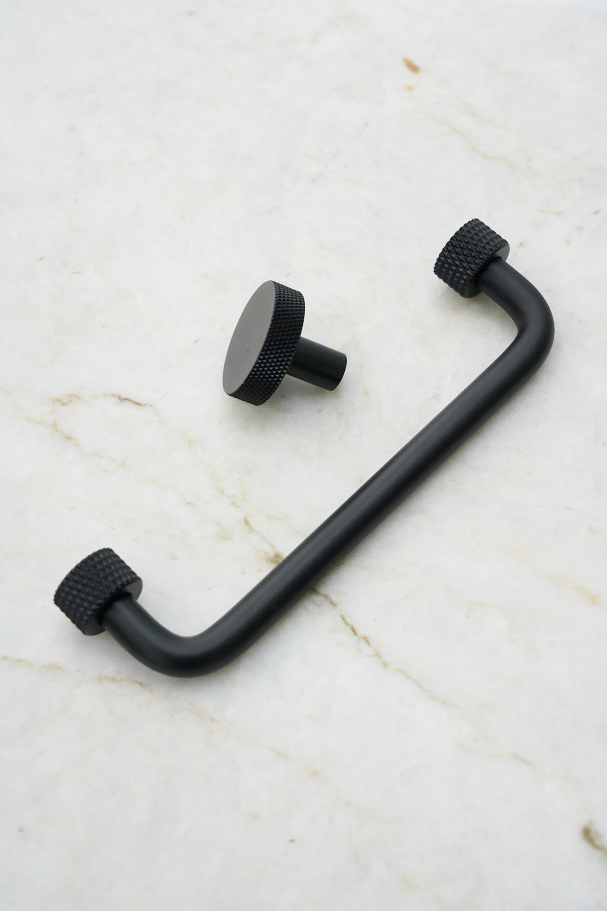 Køkkengreb i massiv messing med en mat sort overflade. Grebet har runde fødder med riflet diamond cut mønster, som matcher til quooker armatur.