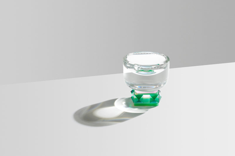 Skål i klar og grøn krystal, på hvidt bord og lysegrå baggrund.